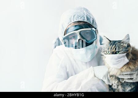 Médecin de l'homme dans des lunettes de protection avec les bras croisés et le chaton de chat est sûr du coronavirus dans le masque de protection médicale. Pandémie mondiale Banque D'Images