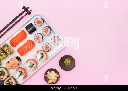 Sushis frais, rouleaux et baguettes sur table rose, Banque D'Images