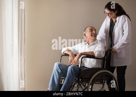 Homme senior assis sur le fauteuil roulant tout en parlant à un médecin. (Santé et forme physique) Banque D'Images