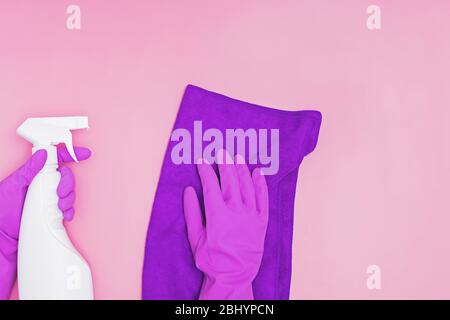 Main féminine dans un gant en caoutchouc tenant le spray de nettoyage et le chiffon sur fond rose. Banque D'Images