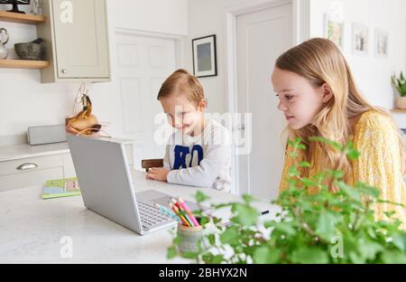 Jeune garçon et fille regardant des vidéos sur un ordinateur portable dans la cuisine. Banque D'Images