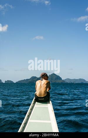 Homme assis sur son dos sur l'arc d'un bateau philippin traditionnel sur une île en train de se hopping à El Nido, Palawan, Philippines Banque D'Images