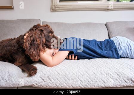 Garçon allongé sur un canapé avec chien de compagnie regardant l'appareil photo. Banque D'Images