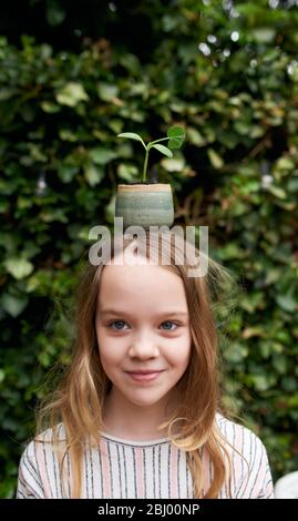 Jeune fille avec pot de plantes sur la tête debout dans le jardin. Banque D'Images