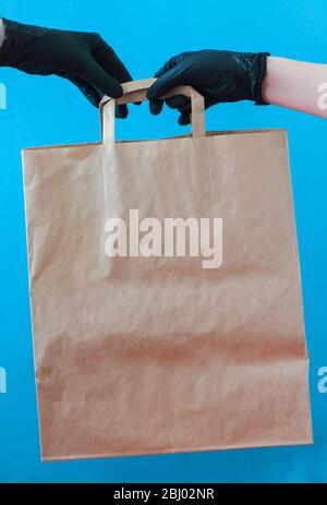 Les mains coupées avec des gants noirs tiennent un sac en papier artisanal. Banque D'Images