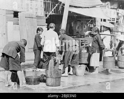 Un millier de personnes sont mortes après un terrible raid aérien à l'aube à Canton, en Chine du Sud, par des avions de bombardement japonais. Beaucoup de bombes ont chuté dans les quartiers les plus pauvres de la ville densément peuplés. Les femmes et les enfants qui s'adparent de l'eau dans le puits public dans un quartier pauvre de Shanghai. L'eau potable est rare et beaucoup de gens partent maintenant en marchant dans les rues. - 23 septembre 1937 Banque D'Images