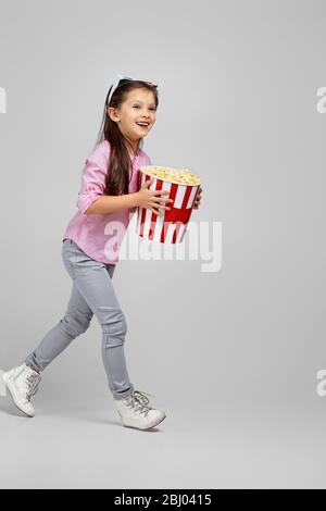 vue sur toute la longueur de la petite fille caucasienne dans des verres tridimensionnels rouge-bleu avec seau à maïs soufflé qui fait mal au cinéma Banque D'Images