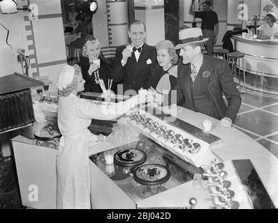 La jeune fille de 17 ans du bar à lait de Londres joue un rôle réel dans les films. - pas beaucoup de gens ont l'occasion de se voir au travail, mais blonde, Marjorie Dale, 17 ans, un agent de bar à lait de Londres, est d'avoir cette expérience. - elle joue la partie d'un bar à lait dans le nouveau film d'Edgar Wallace 'Kate plus Tan' en train d'être fait à Sound City avec Jack Hulbert et Geneviève Tobin en tête. - le réalisateur, le film est tellement content du travail de Marjorie qu'il lui est donné une augmentation de salaire. - spectacles photo, Marjorie Dale vendant des milk shakes à Jack Hulbert et Geneviève à Banque D'Images