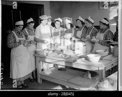 Les femmes sans emploi apprennent à être des cuisiniers cantines à Londres. Comme on s'attend à ce qu'il y ait bientôt une demande considérable de cuisiniers dans les institutions et les cantines, la Commission centrale pour la formation et l'emploi des femmes a ouvert deux centres de Londres où les femmes sans emploi entre 18 et 40 ans peuvent s'entraîner. Les femmes, qui doivent avoir perdu leur emploi à cause de la guerre, subiront un cours de six semaines durant lequel elles seront spécialement formées à la restauration et à la production de repas bon marché et nourrissants dans des conditions de temps de guerre pour un grand nombre. Les étudiantes se réunissent autour d'une table pour l'instruction Banque D'Images