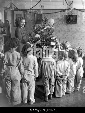 Les enfants s'y marient à côté de l'arbre de Noël pour recevoir un craqueur. - 25 décembre 1947 Banque D'Images