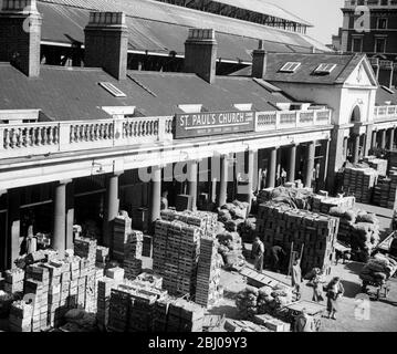 Chariots et boîtes remplis de fruits et légumes dans le marché des fleurs, des fruits et des légumes de Covent Garden . Un panneau donnant des indications vers l' église St Paul , Covent Garden , Londres , est vu sur le bâtiment . Fin des années 1940 , début des années 1950 Banque D'Images