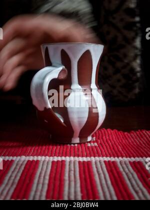 Prendre une tasse de café ou de thé dans un mug en poterie stripey sur une nappe rayée - Banque D'Images