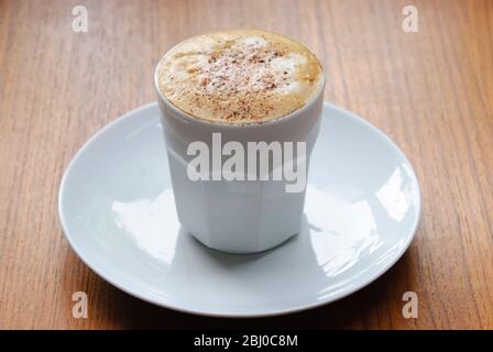 Cappuccino surmonté de mousse dans une tasse sans main avec du cacao dépoli. - Banque D'Images