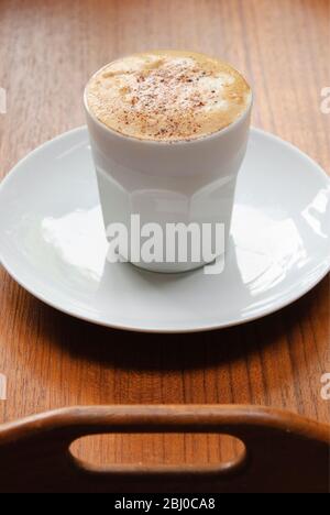 Cappuccino recouvert de mousse dans une tasse blanche sans main sur un plateau en teck marron - Banque D'Images