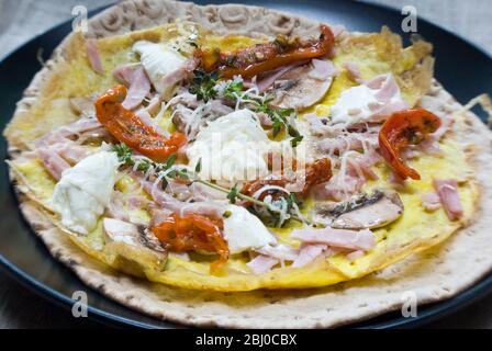 Omelette de style pancake fine avec champignons, jambon, tomates séchées, fromage de chèvre et parmesan sur du pain suédois fin avant d'être roulé, comme une porta Banque D'Images