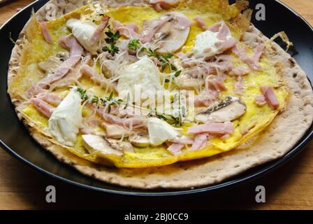 Omelette de style pancake fine avec champignons, jambon, fromage de chèvre et parmesan sur du pain suédois fin avant d'être roulé, comme petit déjeuner portable. - Banque D'Images