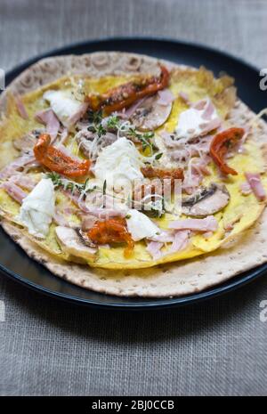 Omelette de style pancake fine avec champignons, jambon, tomates séchées, fromage de chèvre et parmesan sur du pain suédois fin avant d'être roulé, comme une porta Banque D'Images