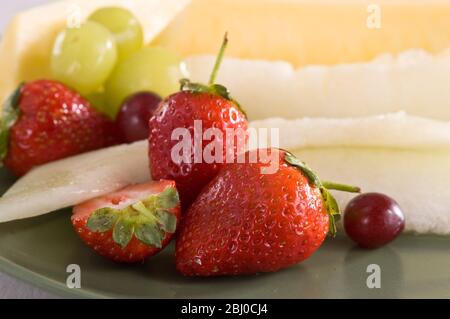 Salade de fruits frais de fraises, raisins et tranches de melon et d'ananas sur la plaque verte. - Banque D'Images