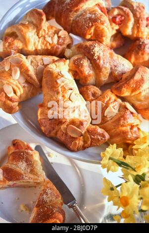Plat de petits croissants, certains sucrés aux amandes effilées, certains salés au jambon et au fromage. - Banque D'Images