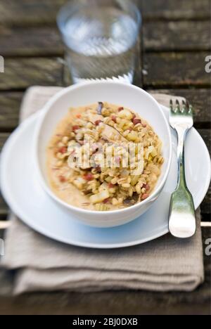 Risotto à l'orge, composé de champignons sauvages séchés, de jambon fumé en dés, d'oignons, de céleri et de bouillon de poulet, servi dans un bol en porcelaine blanche, Outdoor Shot on le Banque D'Images