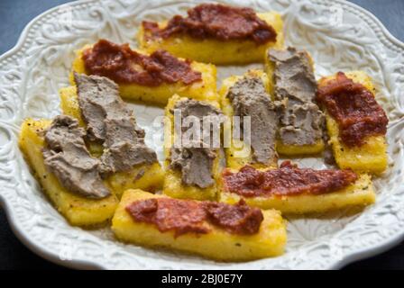 Assiette de crostini faite de polenta frit dans l'huile d'olive, étalée avec du poulet foie ou tartiner de tomates séchées, servie avec des boissons - Banque D'Images