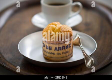 Gâteau de type muffin portugais classique fabriqué avec du riz dans un emballage en papier sur une plaque métallique, avec une tasse de café noir - Banque D'Images