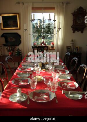 Lumière du soleil brillant à l'intérieur avec une longue table posée pour le repas de Noël avec nappe rouge et la meilleure chine, - Banque D'Images