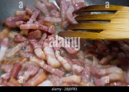 Faire cuire des morceaux de bacon strié dans une poêle. Connu sous le nom de pancetta en Italie et lardons en France - Banque D'Images