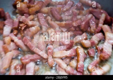 Faire cuire des morceaux de bacon strié dans une poêle. Connu sous le nom de pancetta en Italie et lardons en France - Banque D'Images