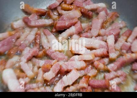 Faire cuire des morceaux de bacon strié dans une poêle. Connu sous le nom de pancetta en Italie et lardons en France - Banque D'Images