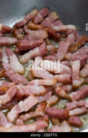 Faire cuire des morceaux de bacon strié dans une poêle. Connu sous le nom de pancetta en Italie et lardons en France - Banque D'Images