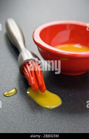 Jaune d'œuf dans un petit bol rouge et gouttes de silicone rouge 'pipis' de la brosse à pâtisserie moderne. - Banque D'Images