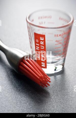 Brosse à pâtisserie moderne avec poils en silicone rouge et un peu de verre mesureur sur surface texturée sombre - Banque D'Images