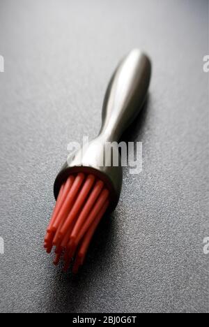 Brosse à pâtisserie moderne avec poils en silicone rouge sur surface texturée sombre - Banque D'Images