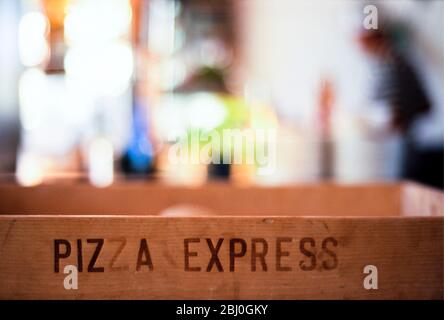 Intérieur du restaurant Pizza Express montrant une boîte de livraison en bois étiquetée et des figures et détails flous en arrière-plan - Banque D'Images