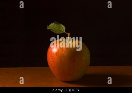 Pomme avec feuille sur surface en bois contre fond noir - Banque D'Images