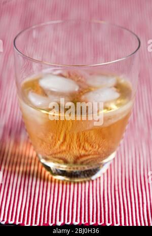 Verre moderne de whisky écossais et d'eau avec glace sur fond rouge rayé - Banque D'Images