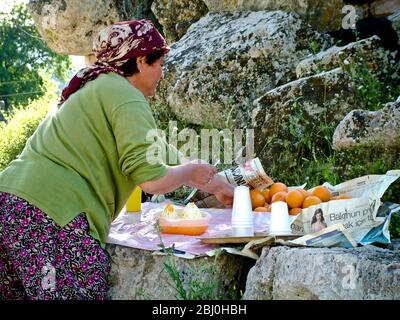 Femme pressant les oranges pour vendre des verres de jus frais aux touristes dans l'ancien amphithéâtre grec, sud de la Turquie - Banque D'Images