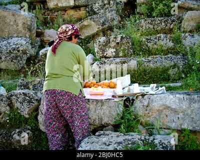 Femme pressant les oranges pour vendre des verres de jus frais aux touristes dans l'ancien amphithéâtre grec, sud de la Turquie - Banque D'Images