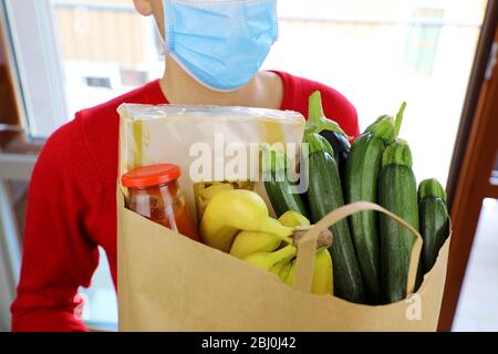 Covid-19 Pandémique Coronavirus Homme avec masque livrer l'ordre de l'épicerie en ligne. Livraison de nourriture pendant l'éclosion du virus corona. Courier portant un masque chirurgical Banque D'Images