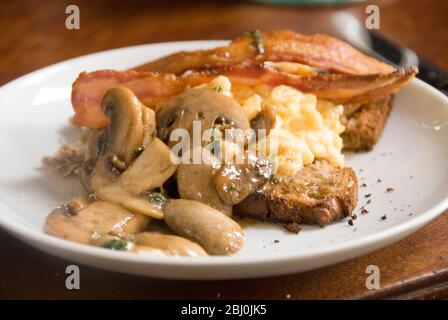 Plaque de petit déjeuner de champignons et œufs brouillés sur pain semé complet avec tranches de bacon et poivre noir fraîchement moulu - Banque D'Images