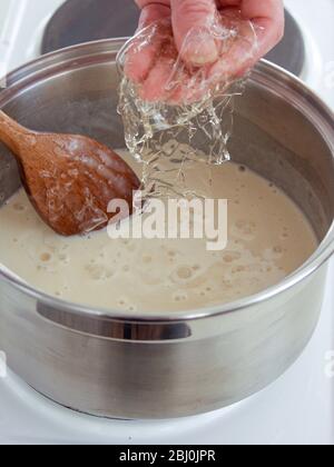Ajouter des feuilles de gélatine ramollies à la crème anglaise pour épaissir et régler - Banque D'Images