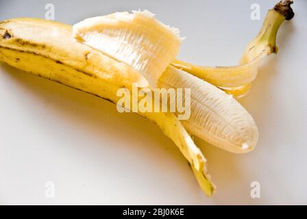 Banane demi-pelée sur surface blanche - Banque D'Images