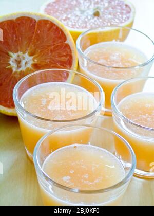 Petits verres de jus de pamplemousse rose avec pamplemousse entier et divisé en deux - Banque D'Images