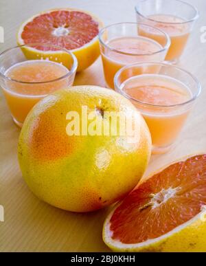 Petits verres de jus de pamplemousse rose avec pamplemousse entier et divisé en deux - Banque D'Images