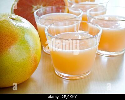 Petits verres de jus de pamplemousse rose avec pamplemousse entier et divisé en deux - Banque D'Images