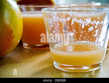 Petits verres de jus de pamplemousse rose avec pamplemousse entier et divisé en deux - Banque D'Images