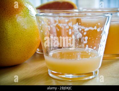 Petits verres de jus de pamplemousse rose avec pamplemousse entier et divisé en deux - Banque D'Images