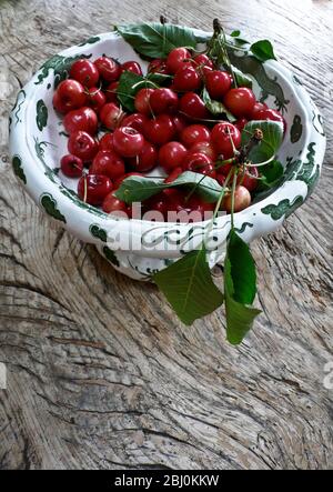 Cerises fraîchement cueillies dans un jardin Kentish dans un bol décoratif sur table en bois rustique - Banque D'Images