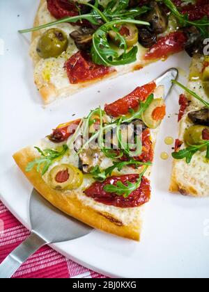 Pizza avec tomates séchées, aubergine, olives, mozzarella et roquette - Banque D'Images